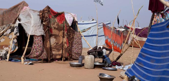 Homme qui se lave grâce a une bassine d'eau au milieu des habitations