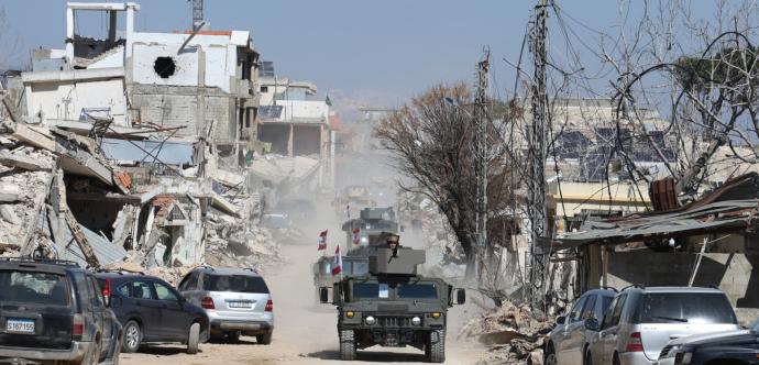 Une ville détruite par des bombes est en arrière plan. On voit des chars militaires sur une route.