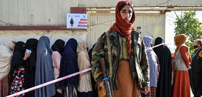 Des femmes voilées sont en arrière-plan, derrière un homme afghan armé