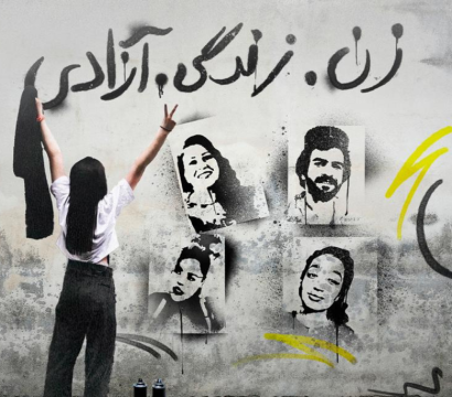 Une femme se tient debout en enlevant son voile devant un graffiti portant l'inscription « Femme, Vie, Liberté »