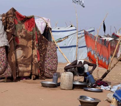 Homme qui se lave grâce a une bassine d'eau au milieu des habitations